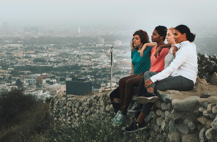 young women friends sitting on wall hill overlooking city