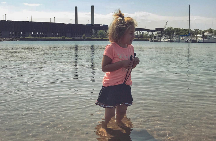 girl stands in water in front of industrial plant