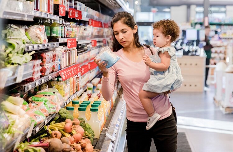 woman with toddler holding grocery vegetable in plastic wrap