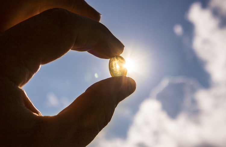 Vitamin D keeps you healthy while lack of sun. Yellow soft shell D-vitamin capsule against sun and blue sky on sunny day. Cure concept.