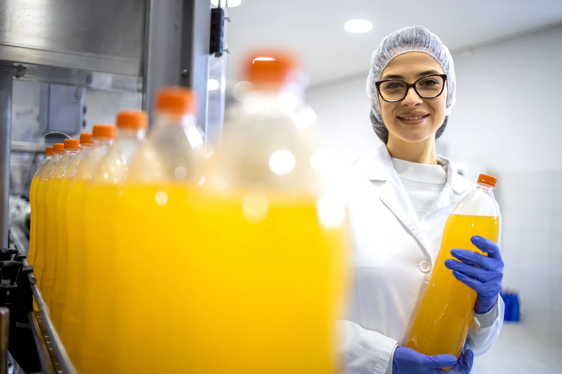 Food-factory-female-supervisor-standing-in-bottling-plant-and-holding-orange-juice-bottle.